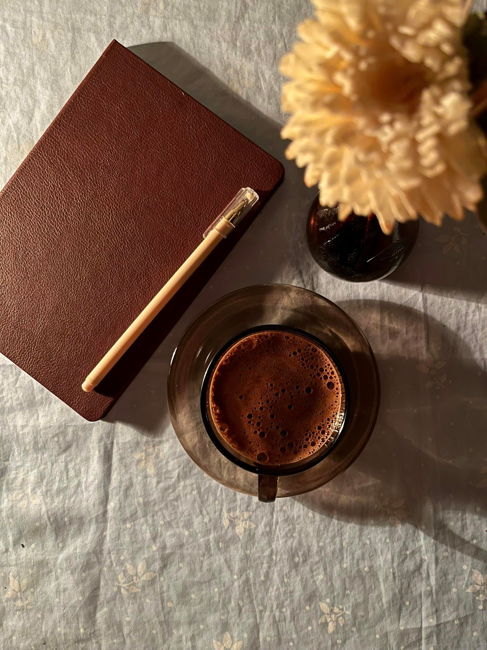 Cozy flat lay of coffee, journal, and flower on table, creating a warm and inviting atmosphere.
